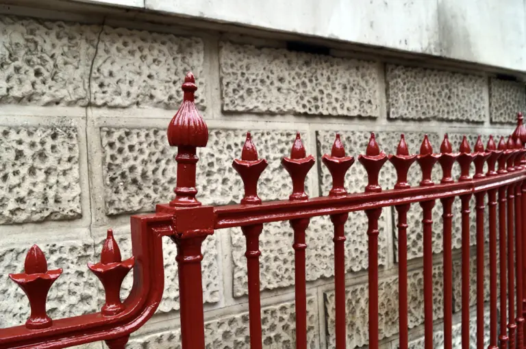 Red metal fence beside a brick wall